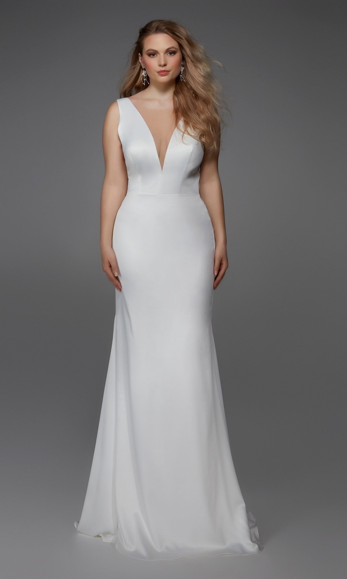 A woman stands against a plain gray background wearing the Alyce 7019—a sleeveless, floor-length white satin dress with a deep V-neckline.